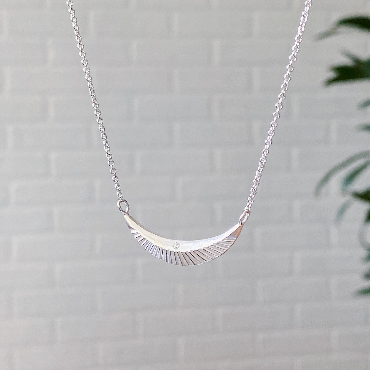 Side view of Crescent necklace with carved rays and a single diamond in sterling silver 
