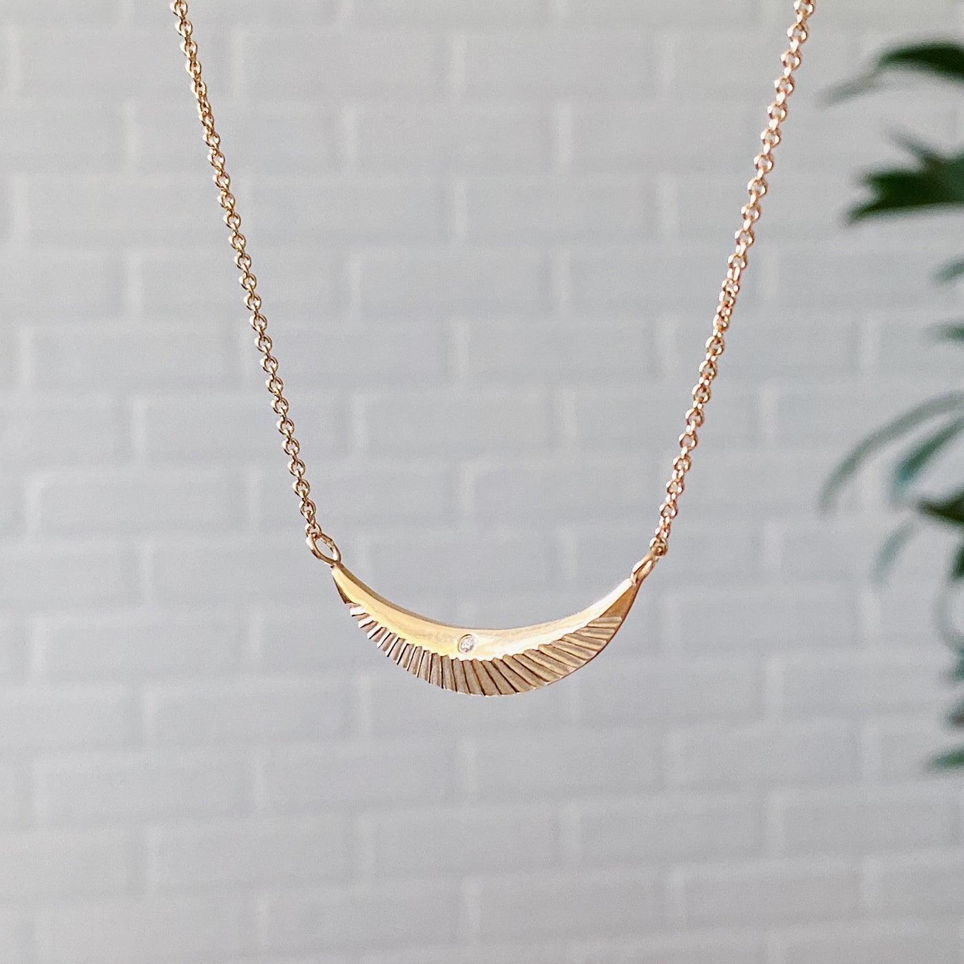 Side view of Crescent necklace with carved rays and a single diamond in vermeil 
