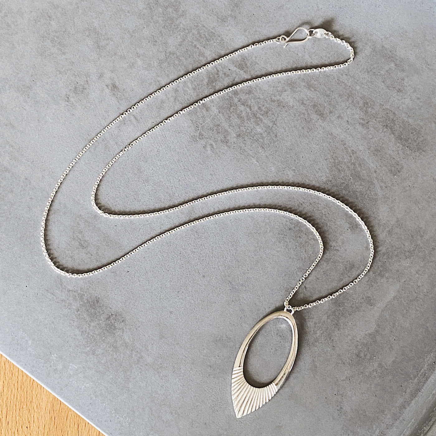 Extra long silver neckalce with large open petal shape pendant with carved ray texture across the bottom