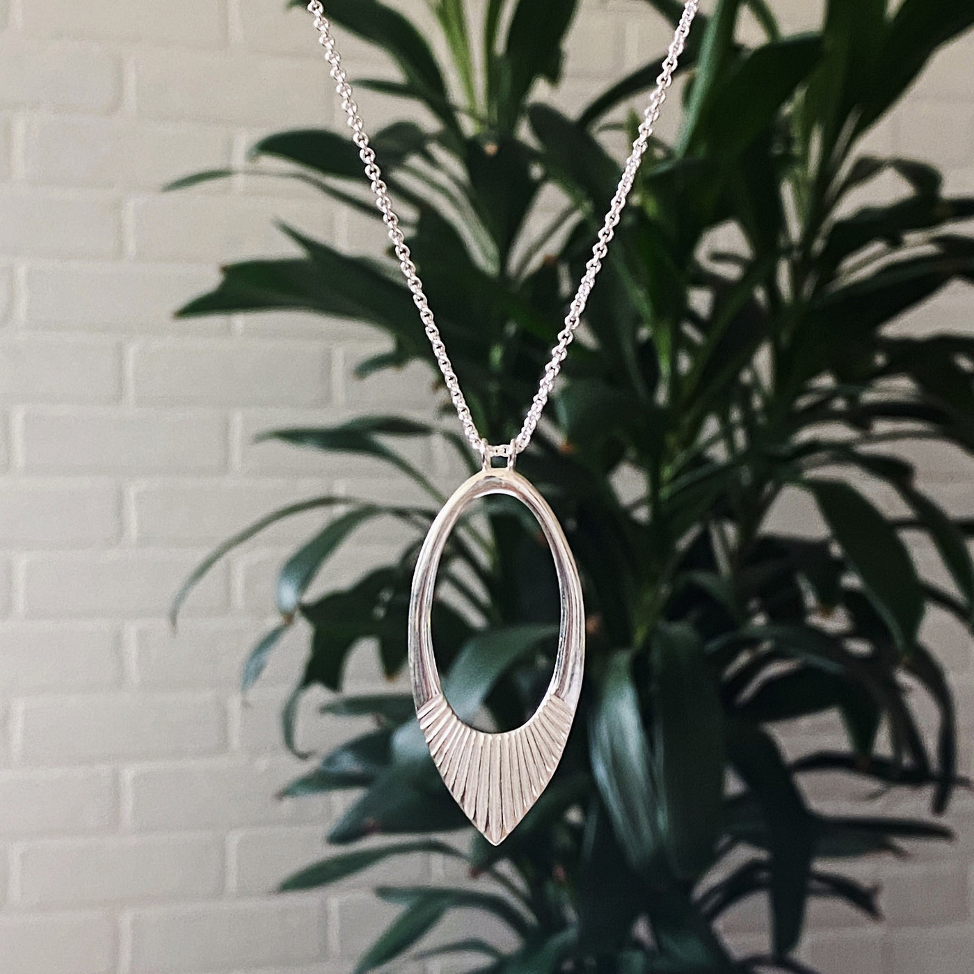 Extra long silver neckalce with large open petal shape pendant with carved ray texture across the bottom