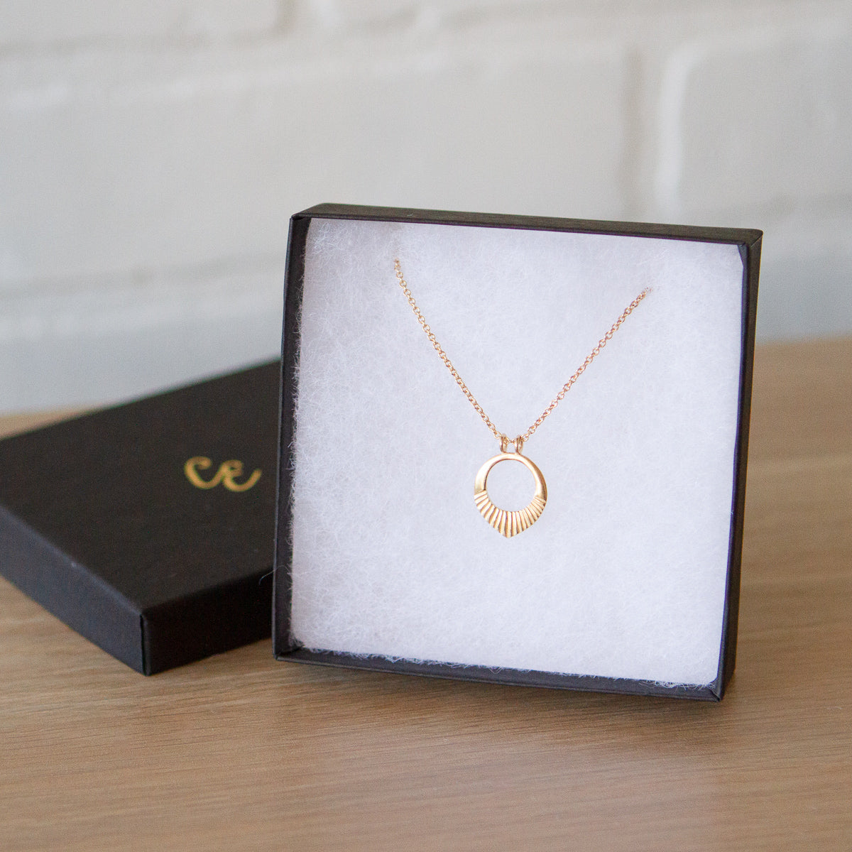 Small vermeil open petal shape necklace with carved rays across the bottom in a gift box