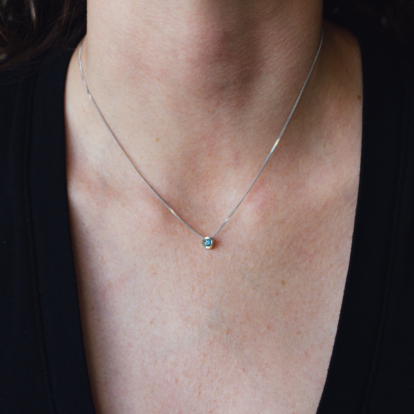 14k white gold small aurora necklace with a blue montana sapphire center around a neck