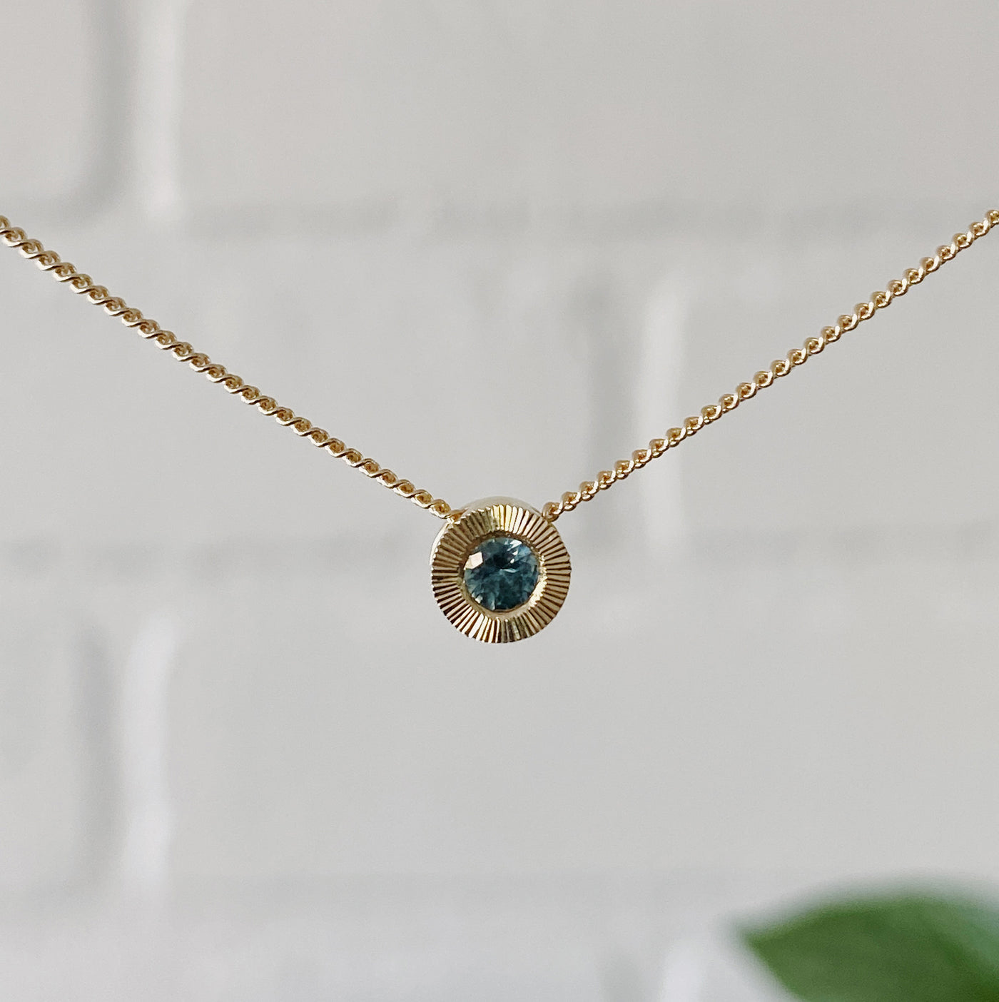 14k yellow gold small aurora necklace with a teal Montana sapphire center in natural light