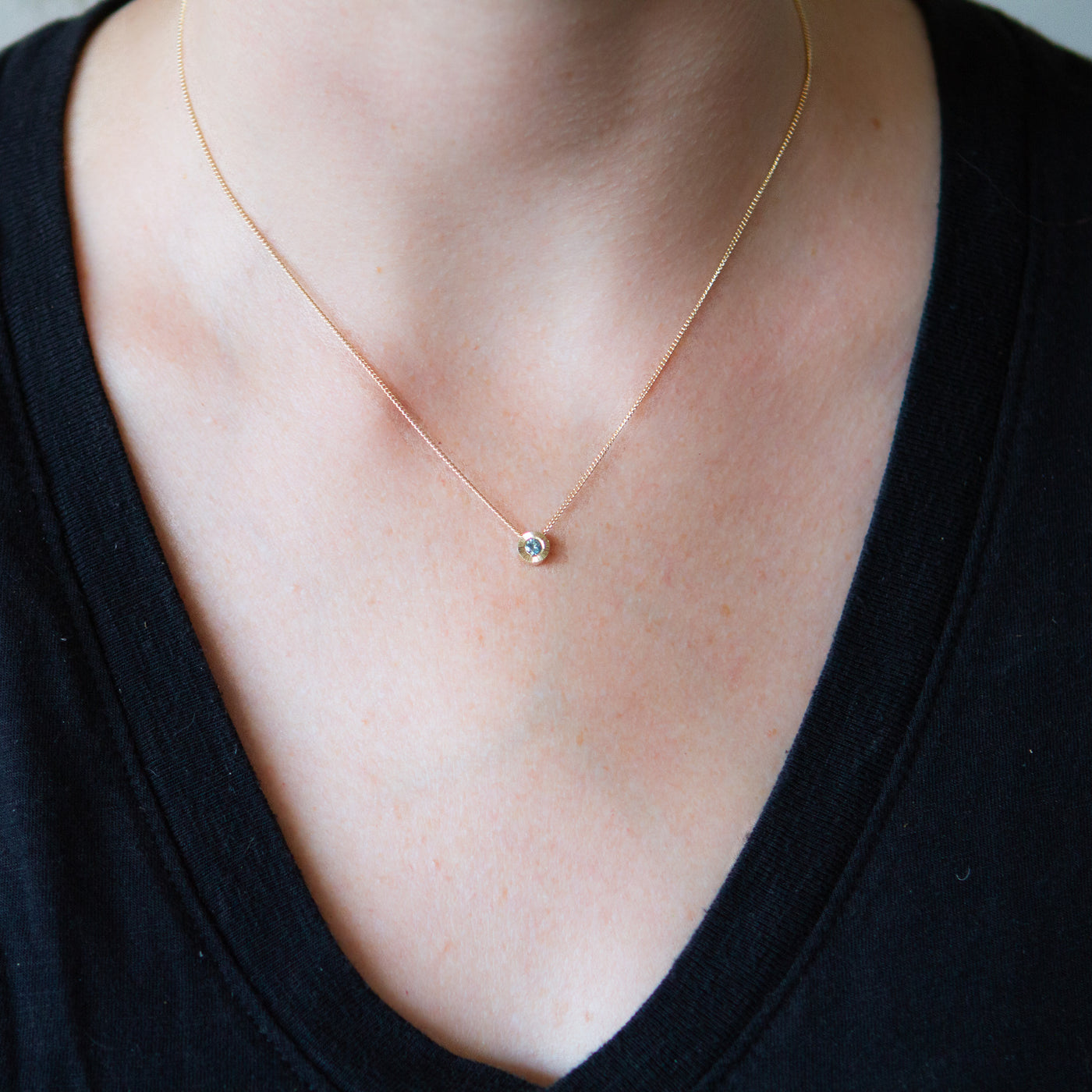 14k yellow gold small aurora necklace with a teal Montana sapphire center around a neck