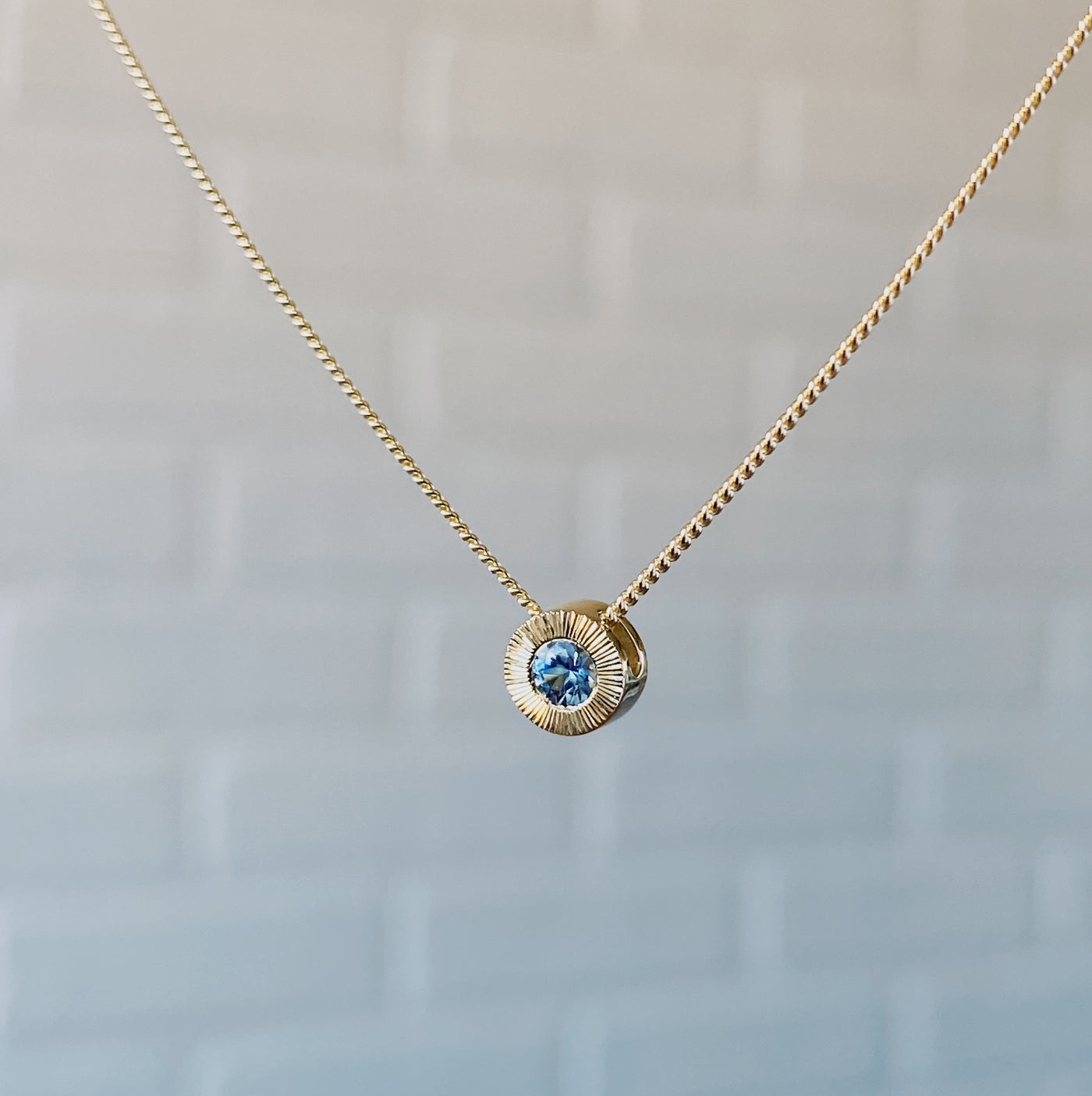 Side view 14k yellow gold small aurora necklace with a denim blue Montana sapphire center in natural light