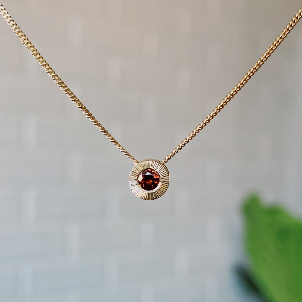January birthstone 14k yellow gold Aurora necklace with garnet center and engraved sunburst halo border.