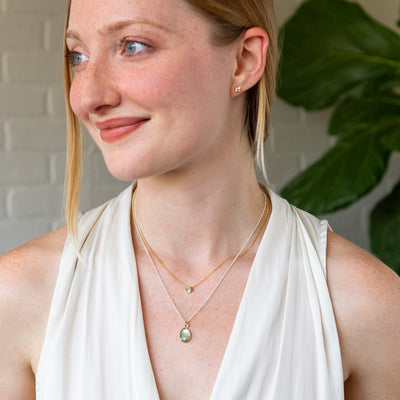 A model wearing a small teal montana sapphire small aurora necklace layered with a green tourmaline theia necklace.