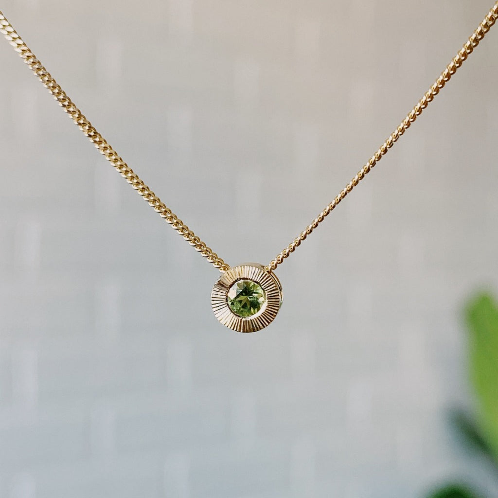 August birthstone 14k yellow gold Aurora necklace with peridot center and engraved sunburst halo border.
