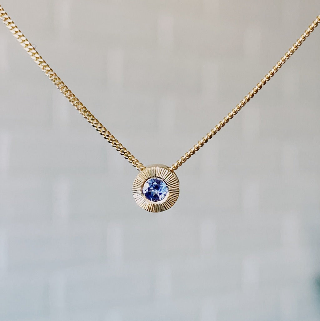 December birthstone 14k yellow gold Aurora necklace with tanzanite center and engraved sunburst halo border.