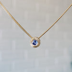 December birthstone 14k yellow gold Aurora necklace with tanzanite center and engraved sunburst halo border.