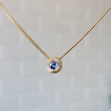 December birthstone 14k yellow gold Aurora necklace with tanzanite center and engraved sunburst halo border.