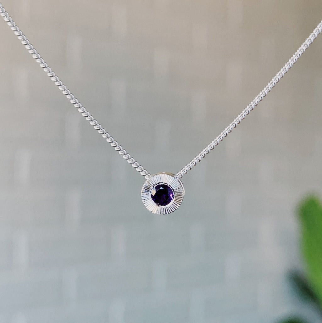 February birthstone sterling silver Aurora necklace with amethyst center and engraved sunburst halo border.