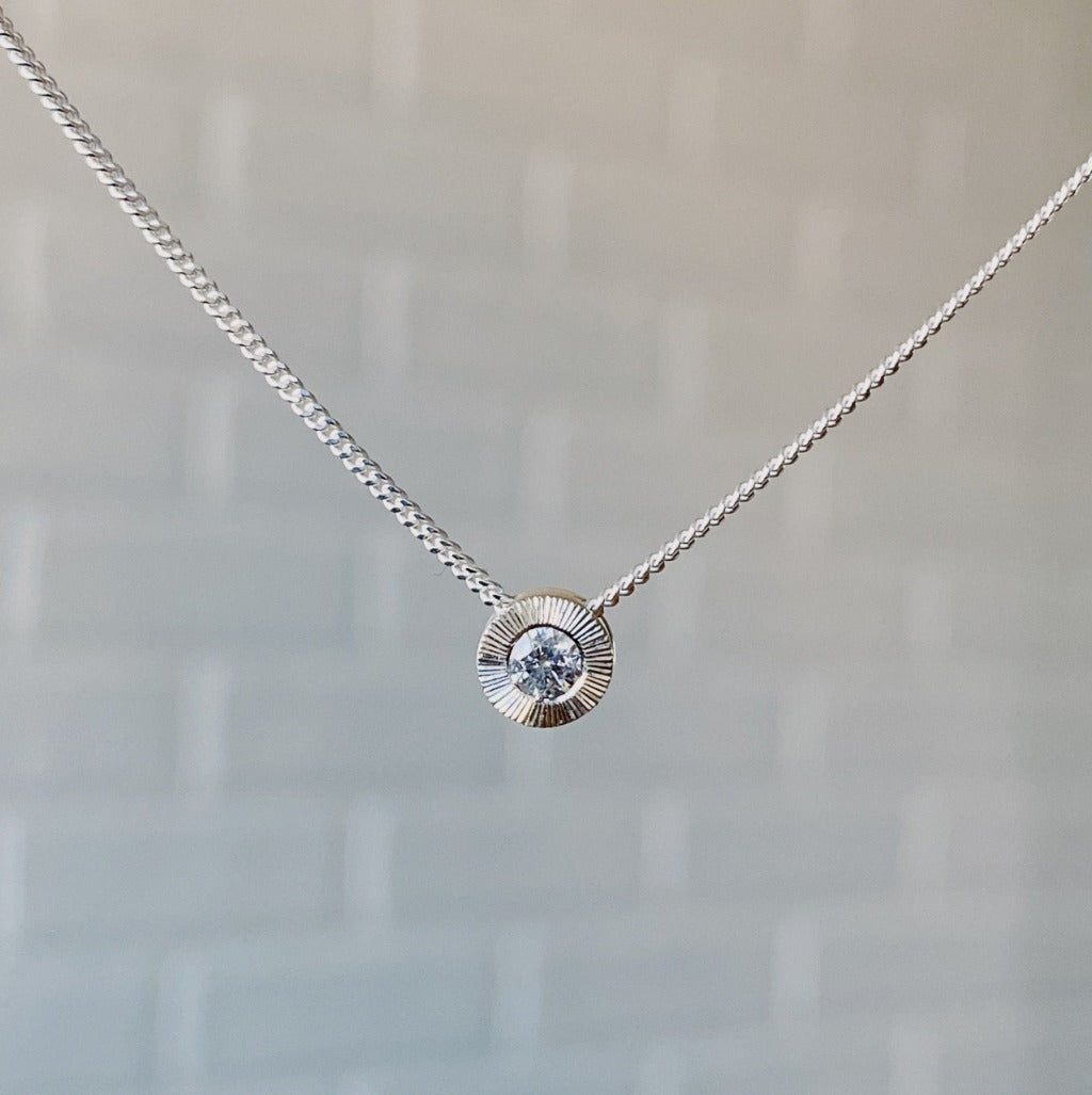 April birthstone sterling silver Aurora necklace with diamond center and engraved sunburst halo border.