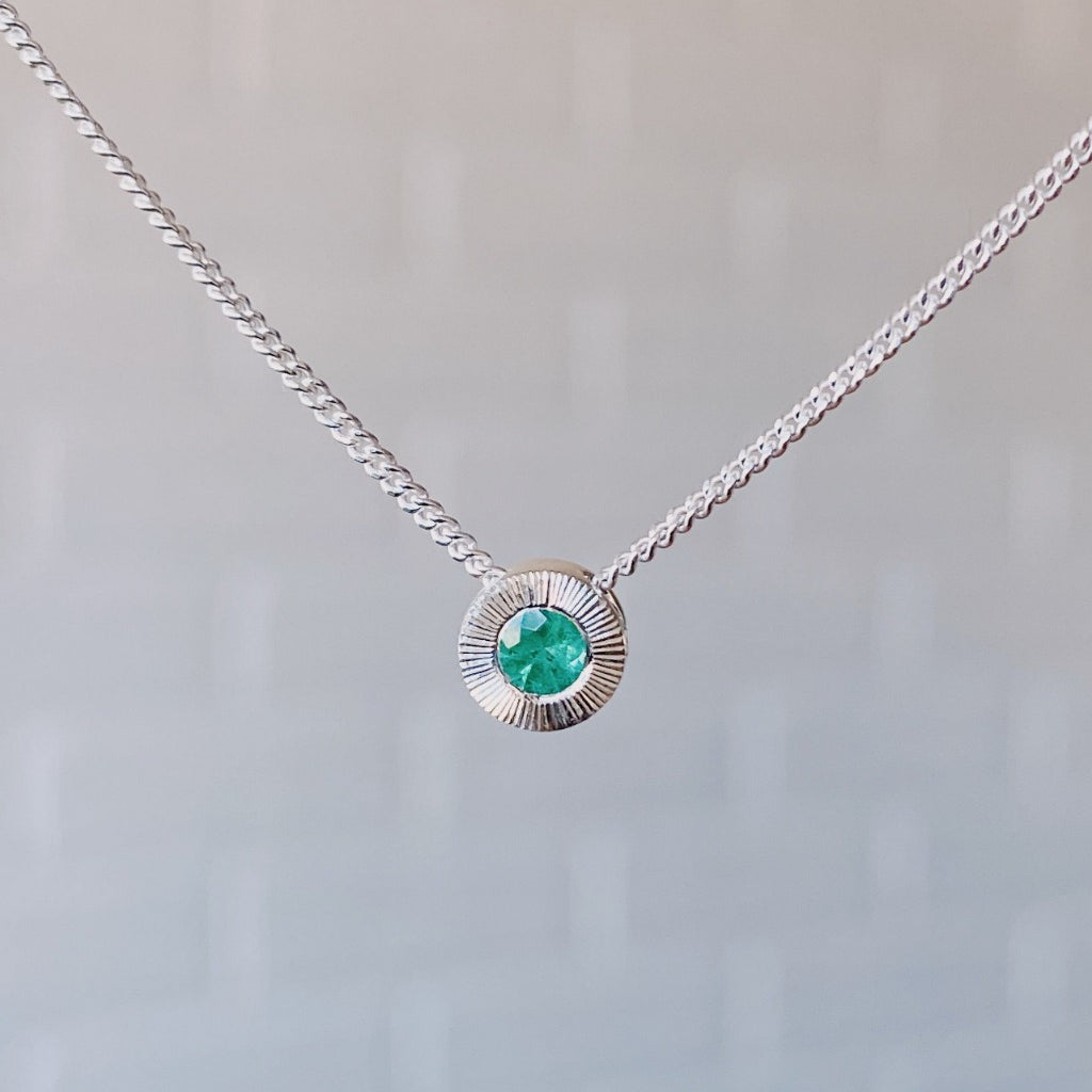 May birthstone sterling silver Aurora necklace with emerald center and engraved sunburst halo border.