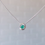 May birthstone sterling silver Aurora necklace with emerald center and engraved sunburst halo border.