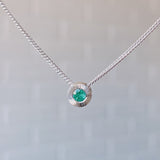 May birthstone sterling silver Aurora necklace with emerald center and engraved sunburst halo border.