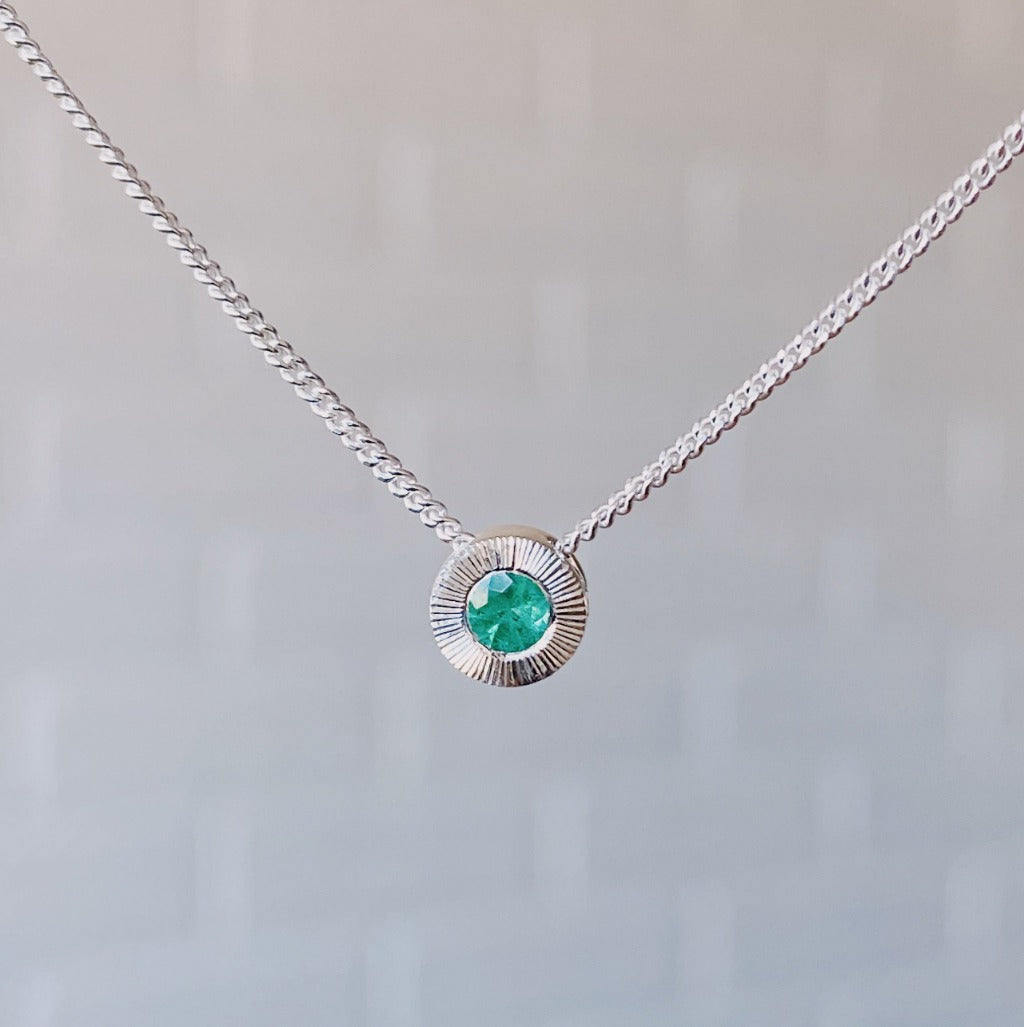 May birthstone sterling silver Aurora necklace with emerald center and engraved sunburst halo border.
