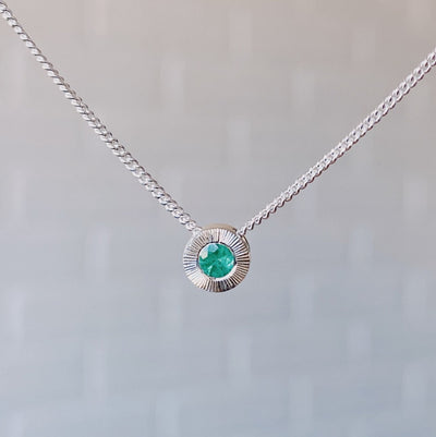 May birthstone sterling silver Aurora necklace with emerald center and engraved sunburst halo border.