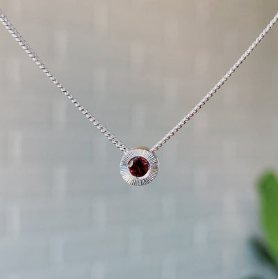 January birthstone sterling silver Aurora necklace with garnet center and engraved sunburst halo border.