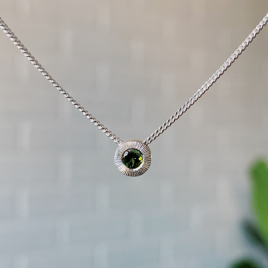 October birthstone sterling silver Aurora necklace with green tourmaline center and engraved sunburst halo border.
