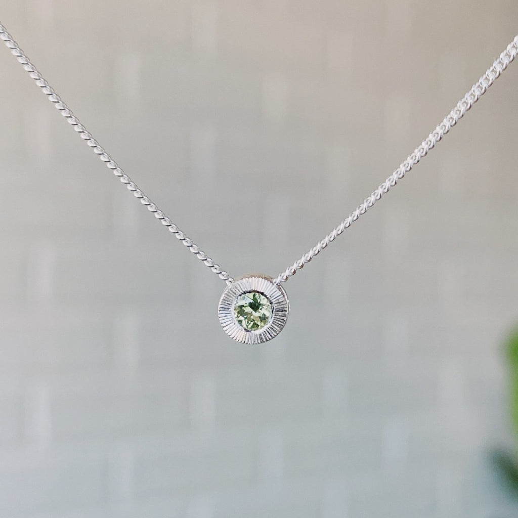 August birthstone sterling silver Aurora necklace with peridot center and engraved sunburst halo border.