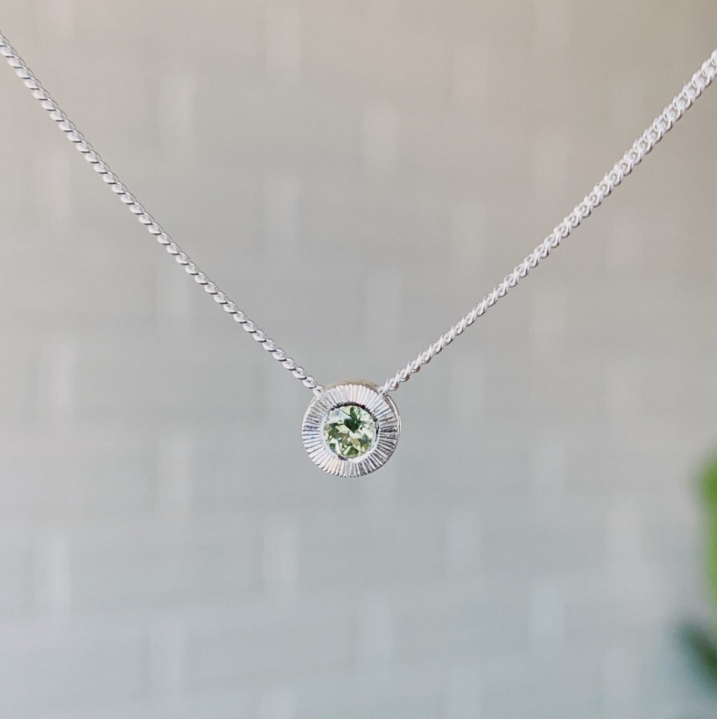 August birthstone sterling silver Aurora necklace with peridot center and engraved sunburst halo border.