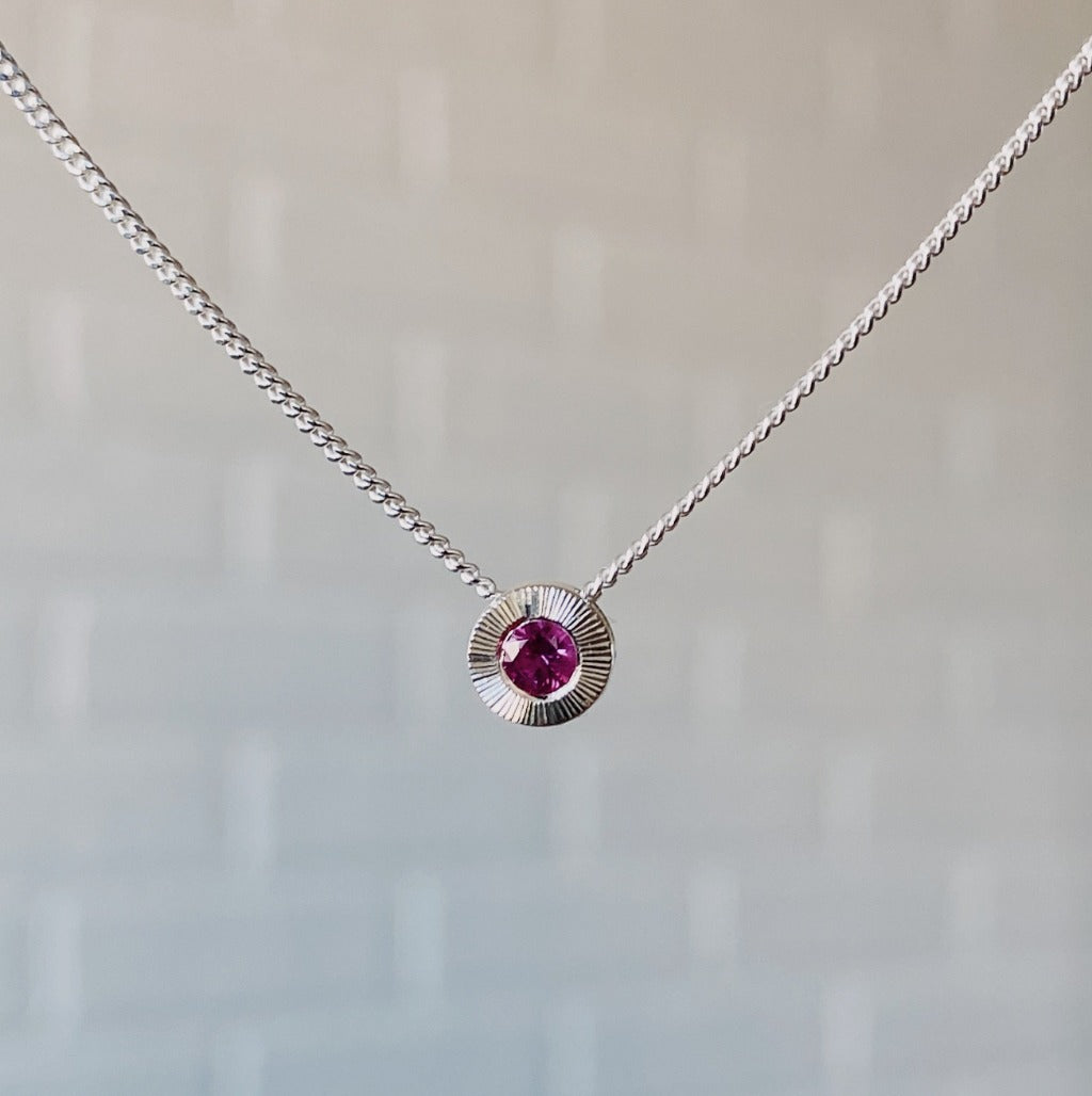 July birthstone sterling silver Aurora necklace with ruby center and engraved sunburst halo border.