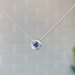 December birthstone sterling silver Aurora necklace with tanzanite center and engraved sunburst halo border.