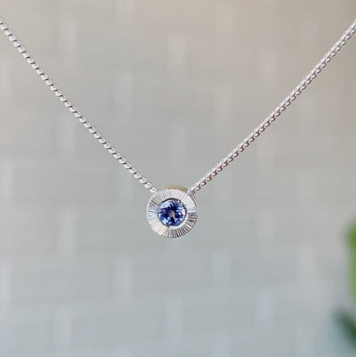 December birthstone sterling silver Aurora necklace with tanzanite center and engraved sunburst halo border.