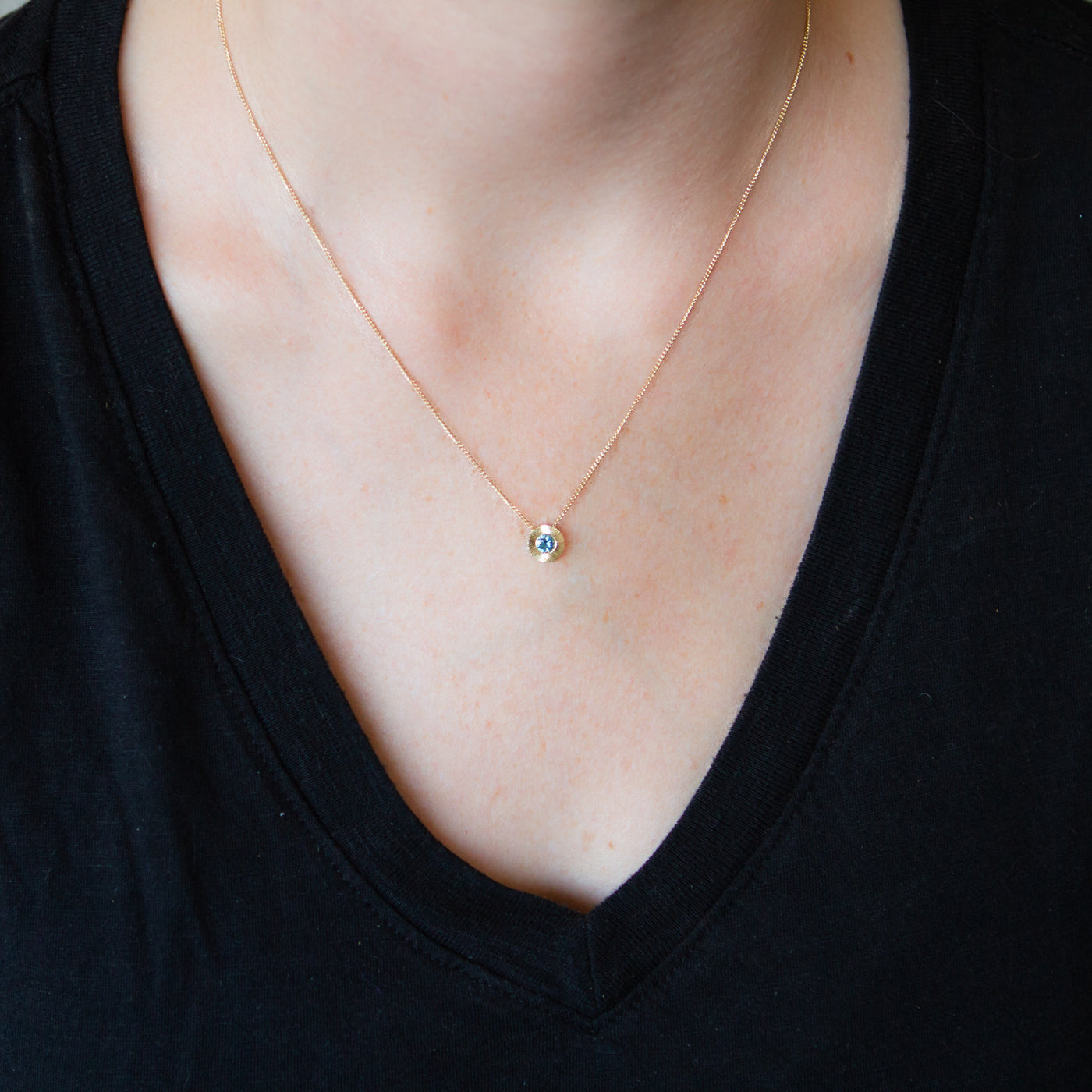 14k yellow gold Medium aurora necklace with a light teal Montana sapphire center around a neck