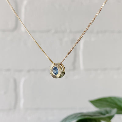 Side view 14k yellow gold Medium aurora necklace with a denim blue Montana sapphire center and engraved halo border in natural light