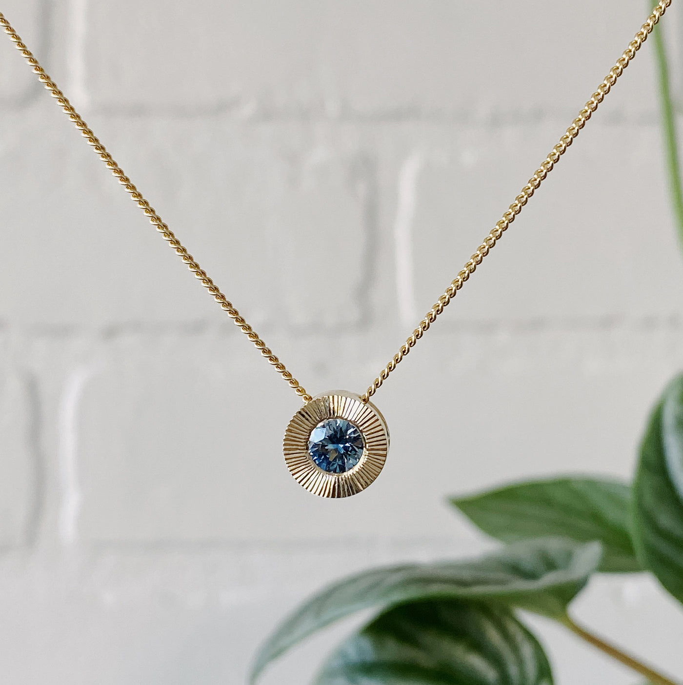 14k yellow gold large aurora necklace with a denim blue Montana sapphire center and engraved halo border in natural light