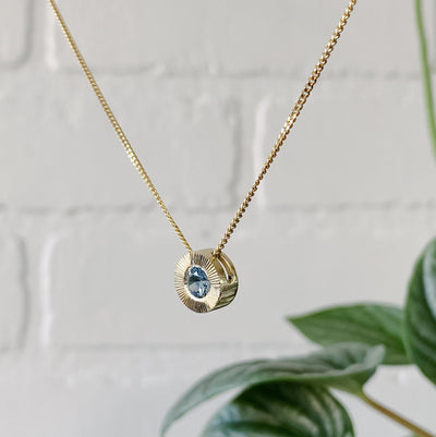Side view 14k yellow gold large aurora necklace with a denim blue Montana sapphire center and engraved halo border in natural light