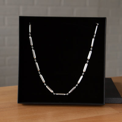 Fragment Link Necklace in Silver on a wooden table in packaging 