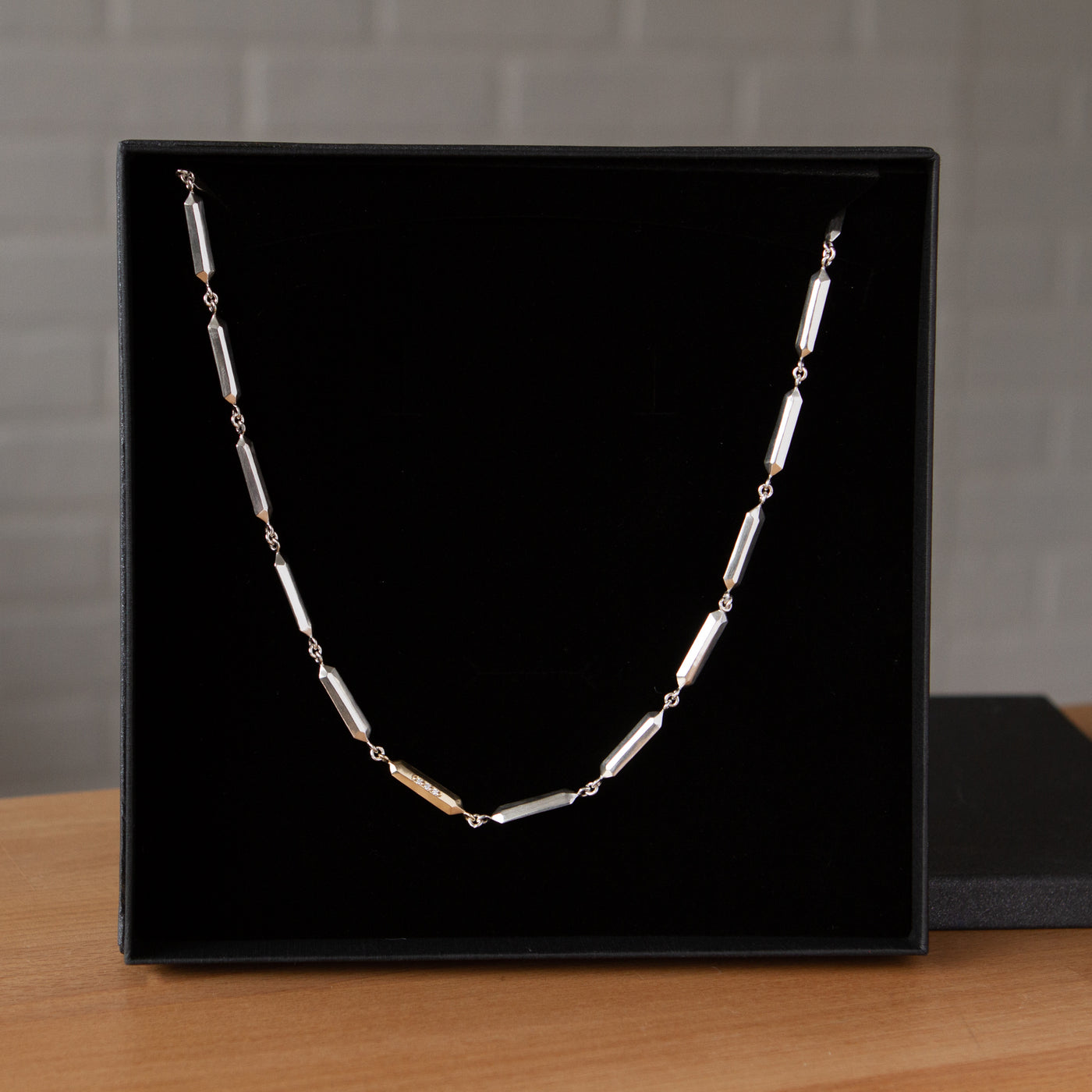Fragment Link Necklace with Gold Link on a wooden table in packaging 