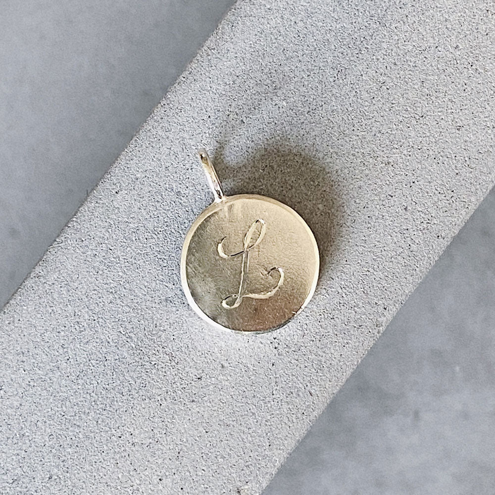 Round sterling silver pendant with a hand-engraved script "L" initial letter