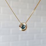 14k yellow gold Medium aurora necklace with a light teal Montana sapphire center in natural light
