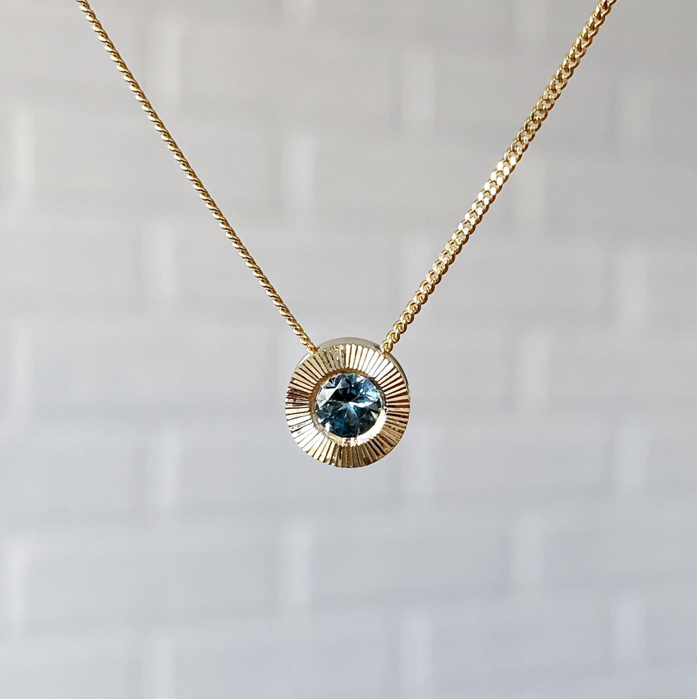 14k yellow gold Medium aurora necklace with a light teal Montana sapphire center in natural light