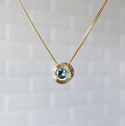 Side View 14k yellow gold Medium aurora necklace with a light teal Montana sapphire center in natural light