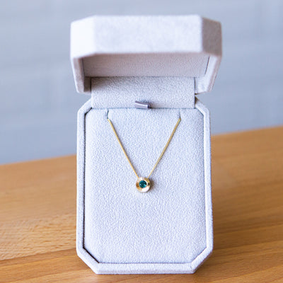 14k yellow gold medium Aurora necklace with a round teal green indicolite tourmaline center and engraved rays halo border in a gift box