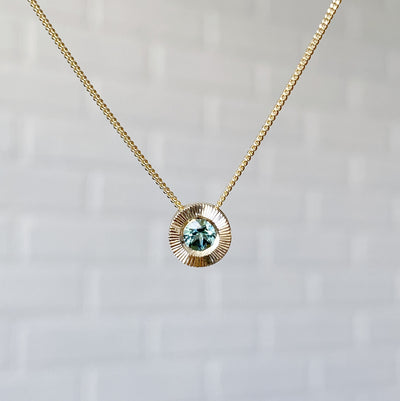 14k yellow gold medium Aurora necklace with a round seafoam green tourmaline center and engraved rays halo border in natural light