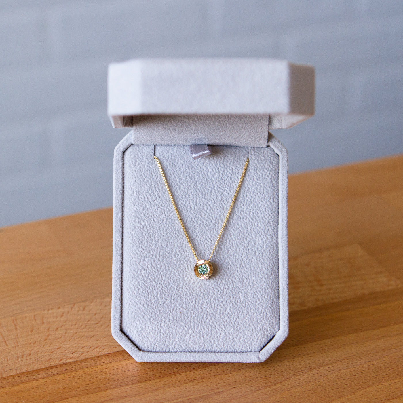 14k yellow gold medium Aurora necklace with a round seafoam green tourmaline center and engraved rays halo border in a gift box
