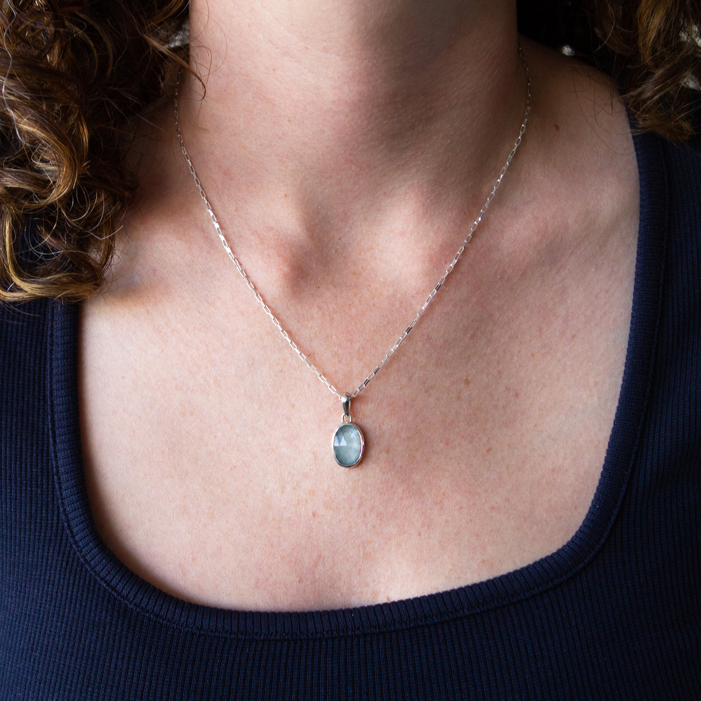 Oval Rose cut cloudy aquamarine in a sterling silver bezel pendant with a faceted silver bail on an elongated box chain around a neck