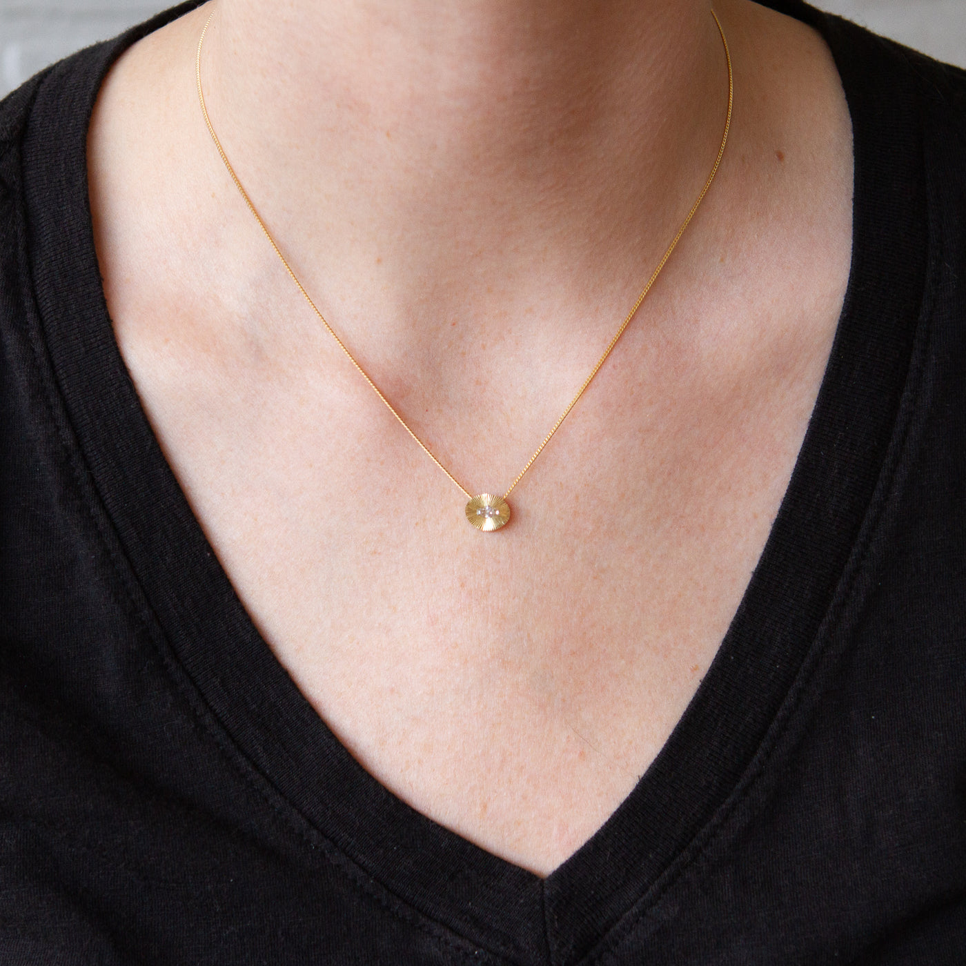 Antique step-cut diamond in a yellow gold oval aurora pendant with engraved rays on an 16" chain around a neck.