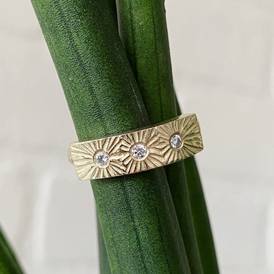 Yellow gold bar ring with three diamonds and a carved sunburst design around each by Corey Egan in natural light