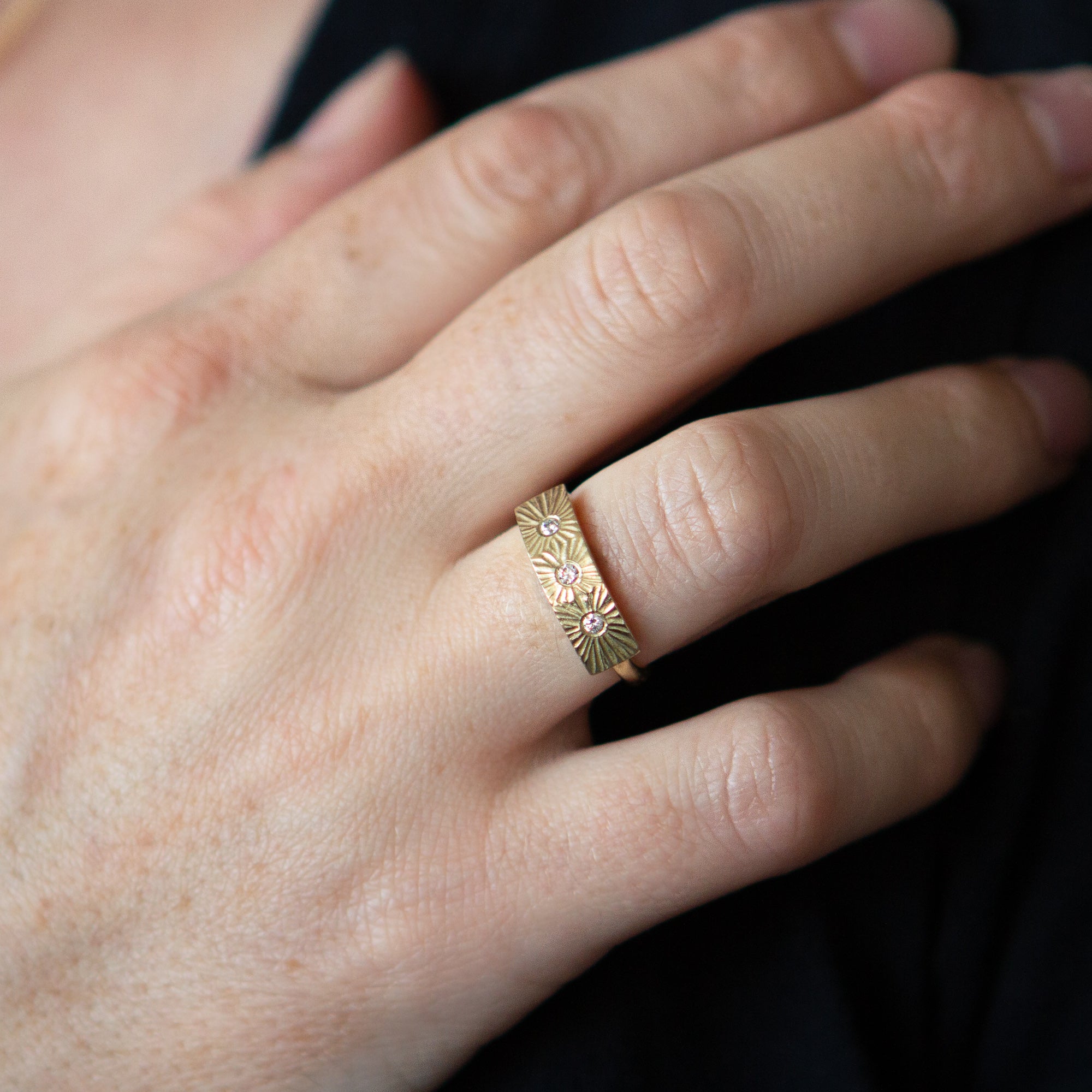 Yellow gold bar ring with three diamonds and a carved sunburst design around each by Corey Egan on a hand