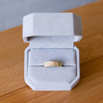 Yellow gold bar ring with three diamonds and a carved sunburst design around each by Corey Egan in a ring box