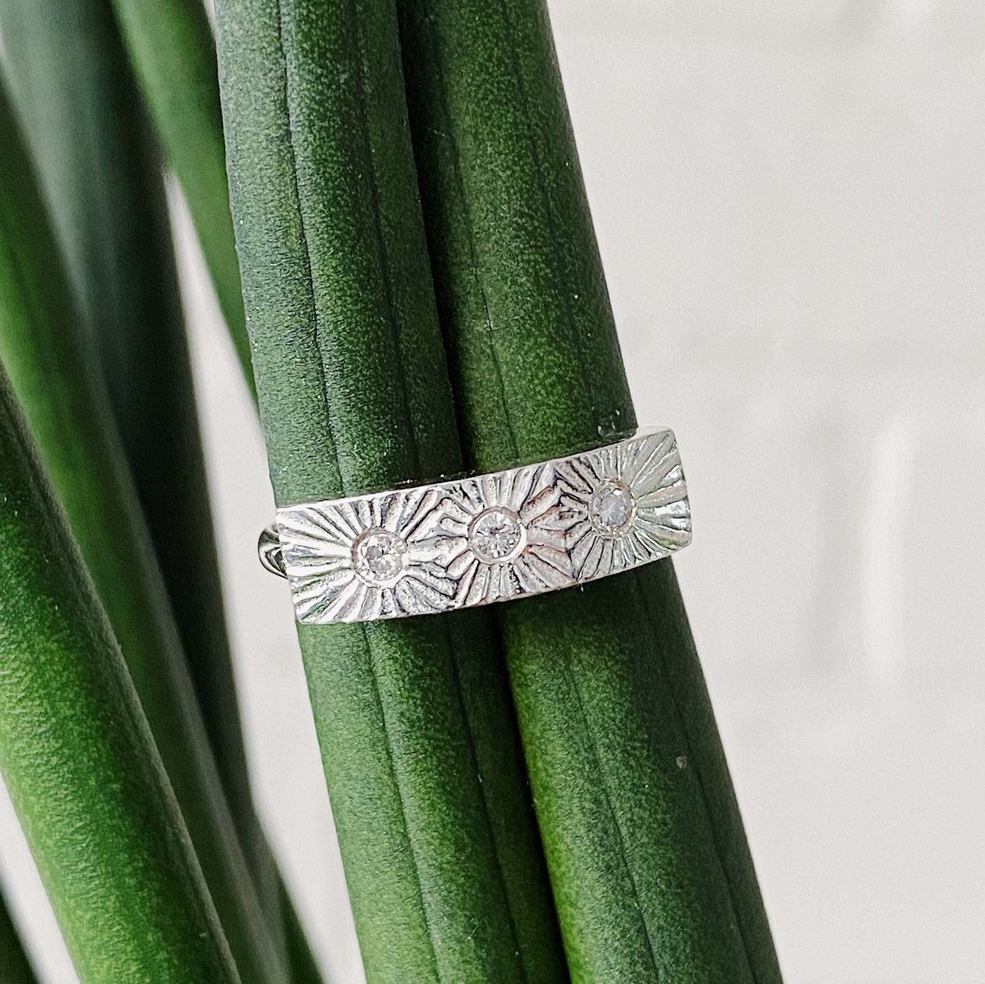 Sterling silver bar ring with three diamonds and a carved sunburst design around each by Corey Egan in natural light