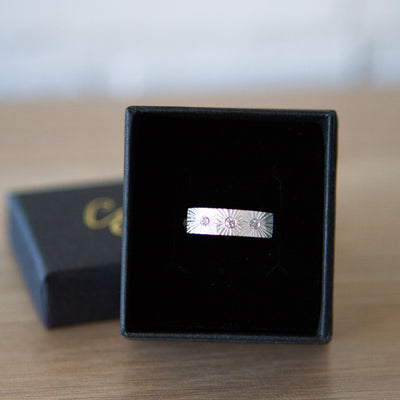 Sterling silver bar ring with three diamonds and a carved sunburst design around each by Corey Egan in a ring box