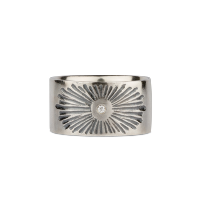 Oxidized silver wide band with single diamond and a carved sunburst design on a white background by Corey Egan